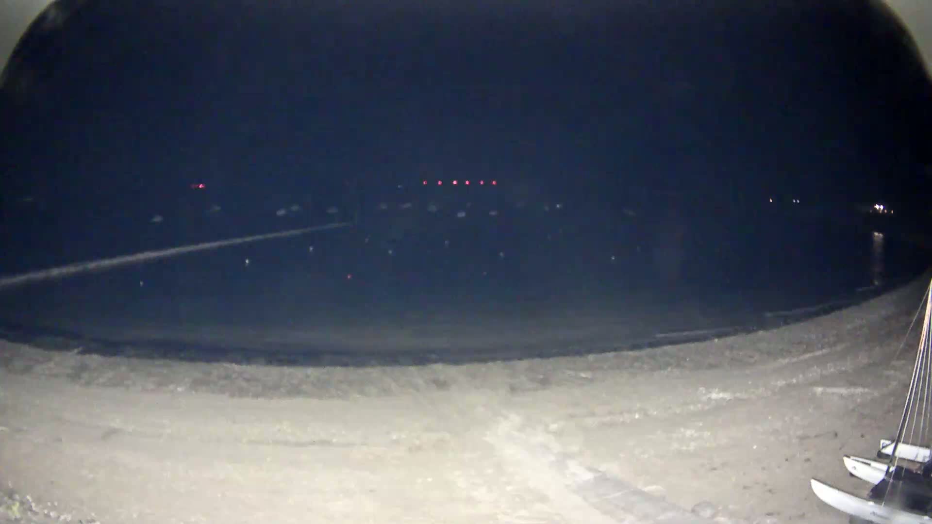 A dark, nighttime beach scene shows two catamarans on the sand with faint lights visible across the water.