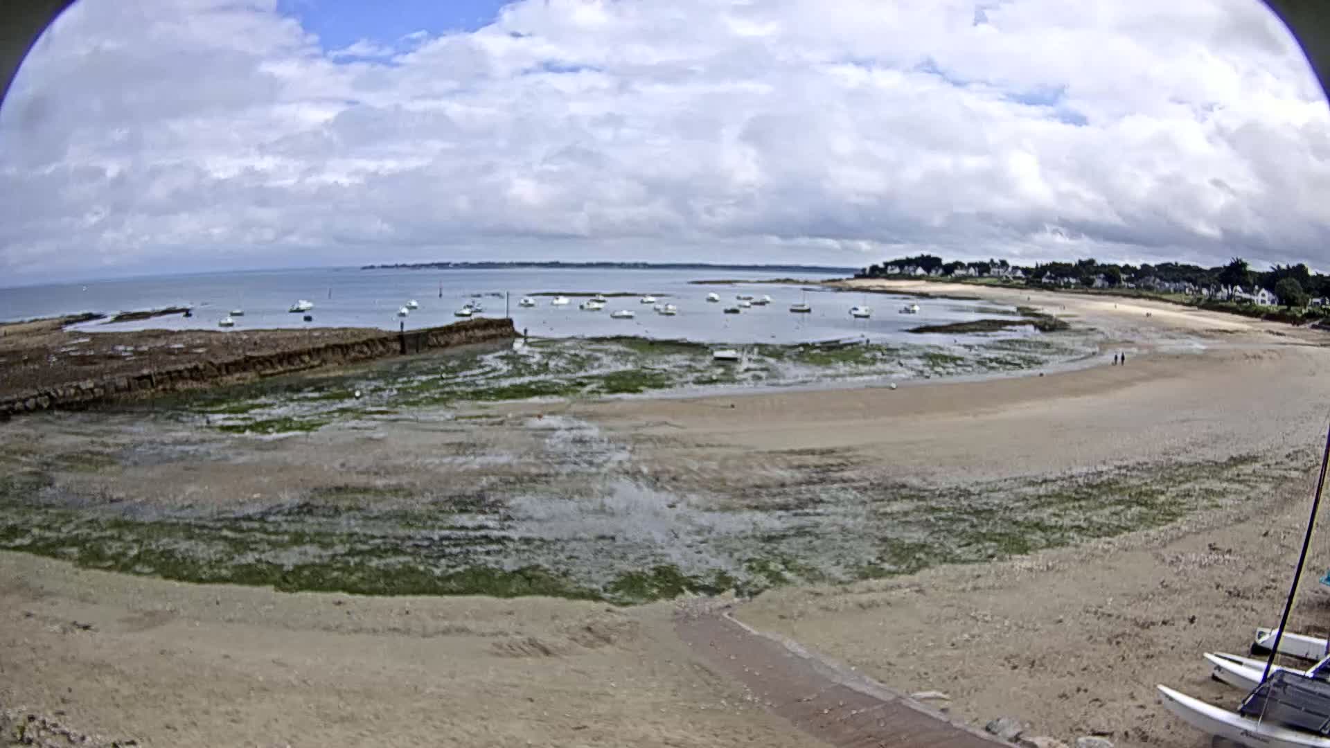 A sandy beach with several small boats in the water under a partly cloudy sky.