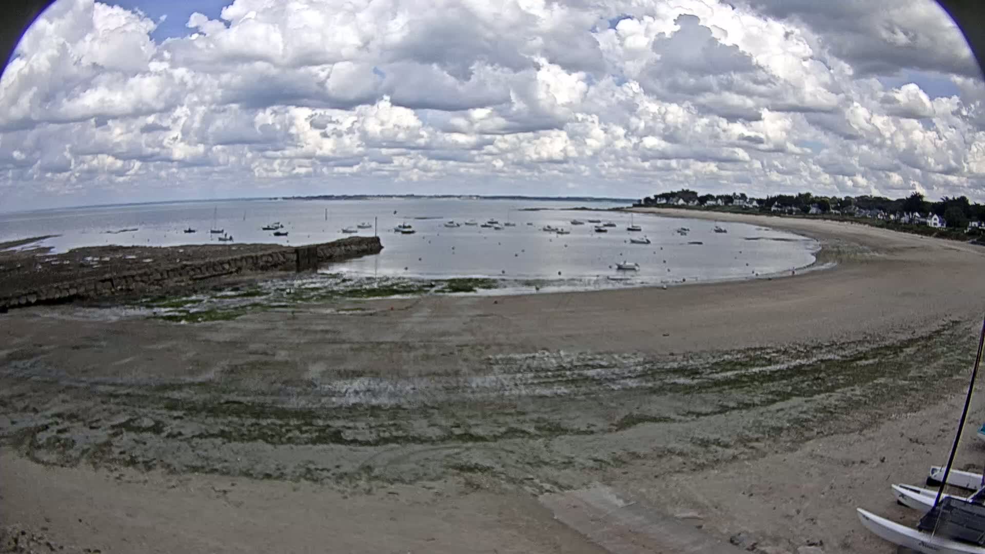 A sandy beach with several boats in the calm water under a partly cloudy sky.