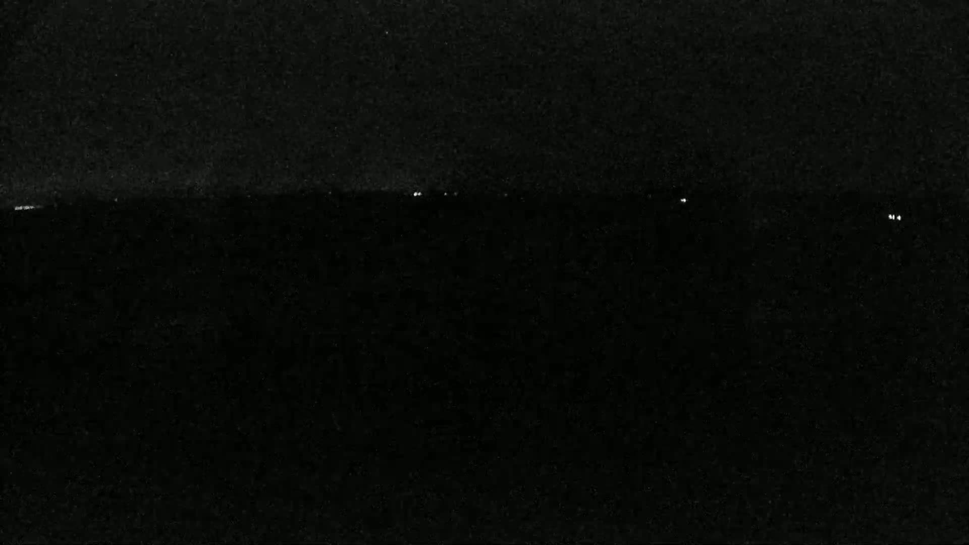 A nighttime view shows a dark landscape with a few faint lights on the horizon.
