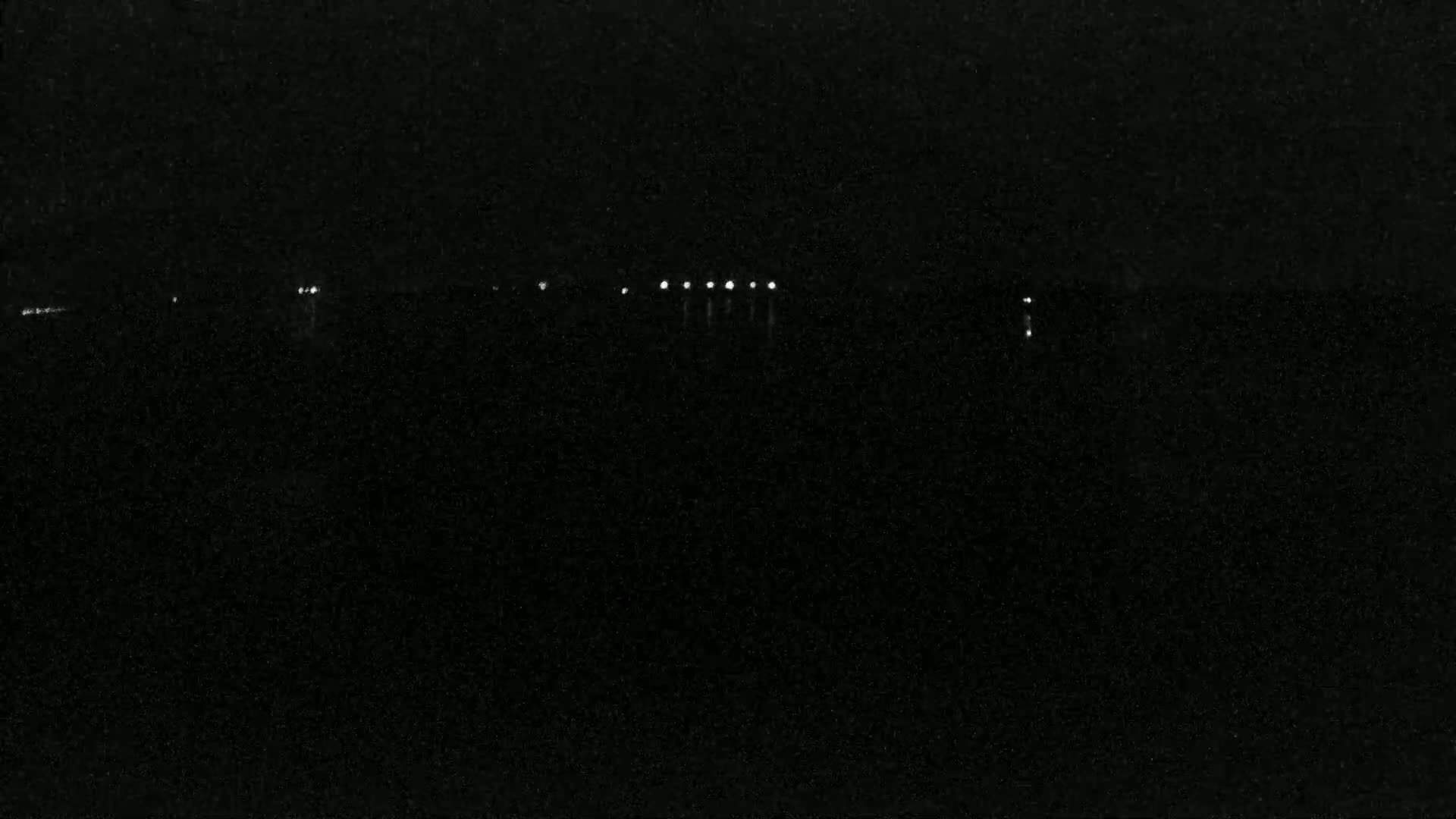 A dark, nighttime scene shows a line of distant lights across a black landscape.