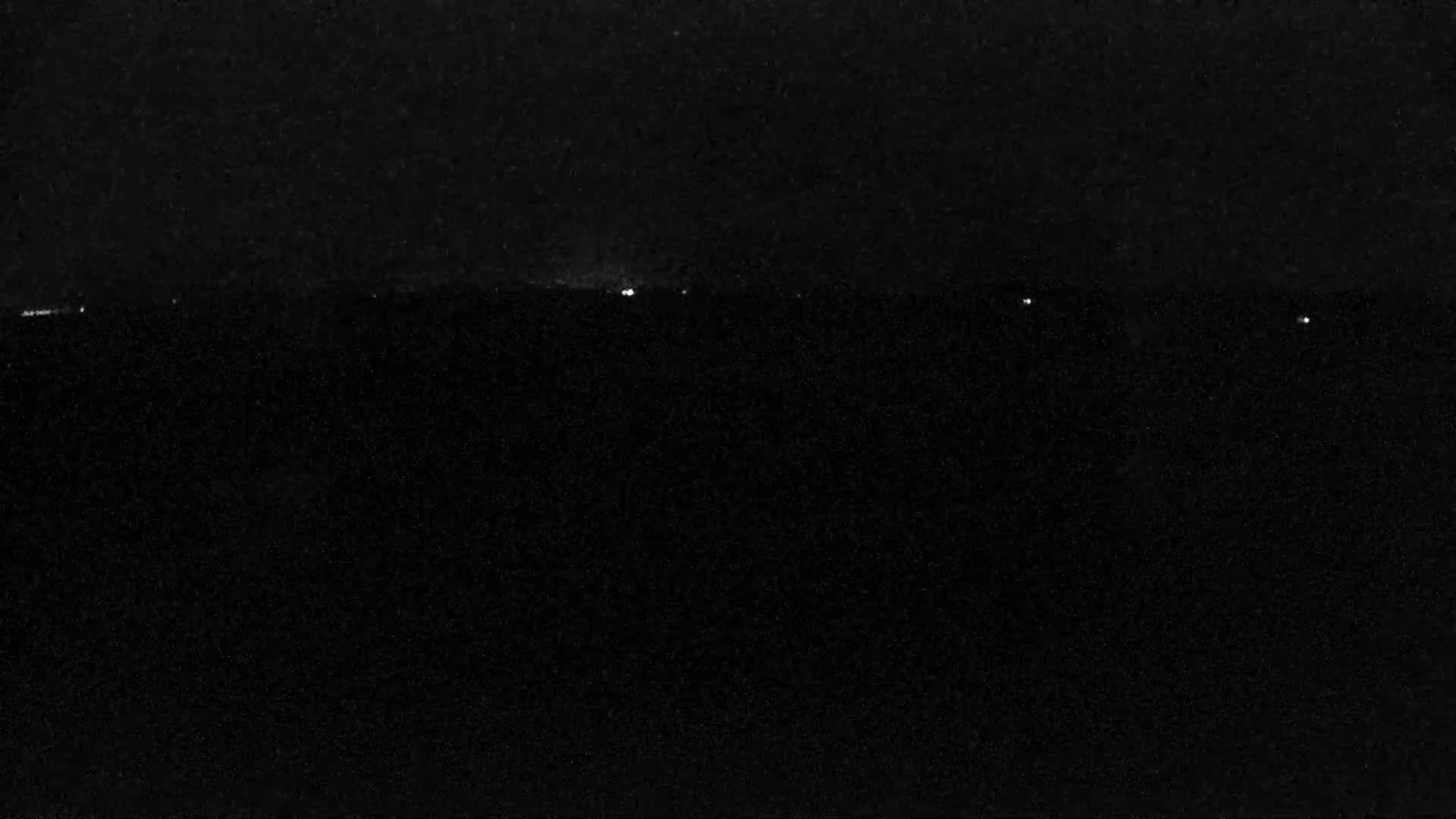 A nighttime image shows a dark, possibly hazy or dusty, landscape with a few faint lights visible on the horizon.