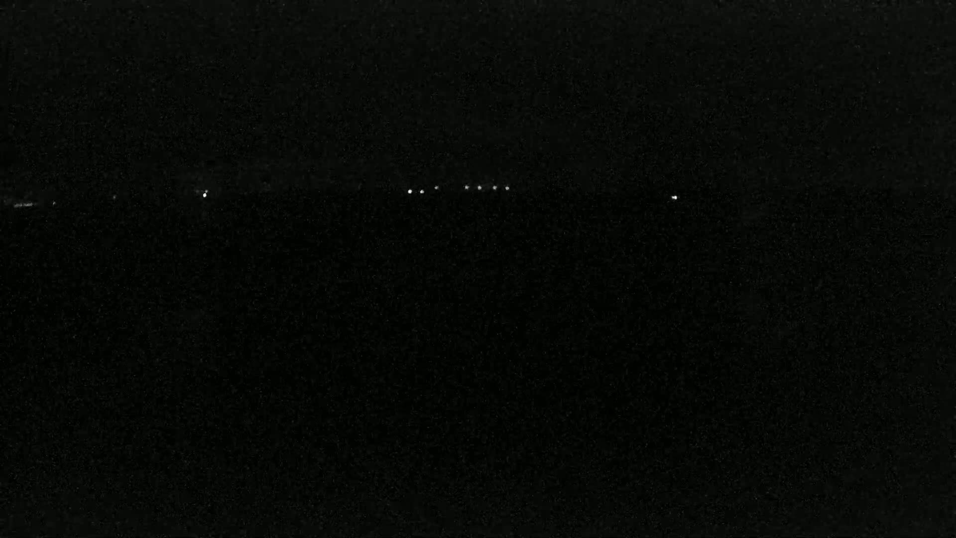 A nighttime, dark image shows a line of small, faint lights in the distance.