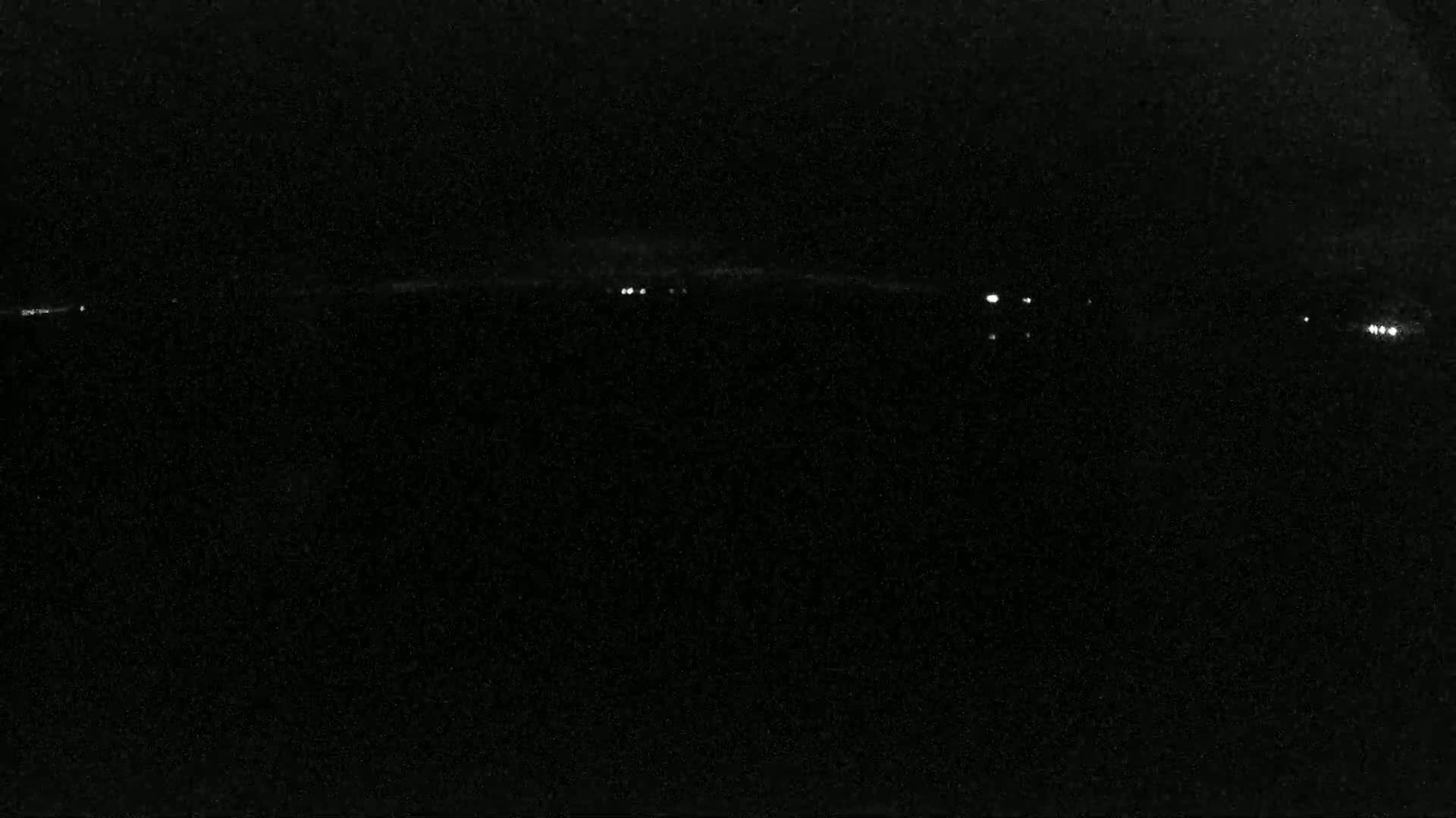 A dark, nighttime landscape with a few distant lights visible on the horizon.