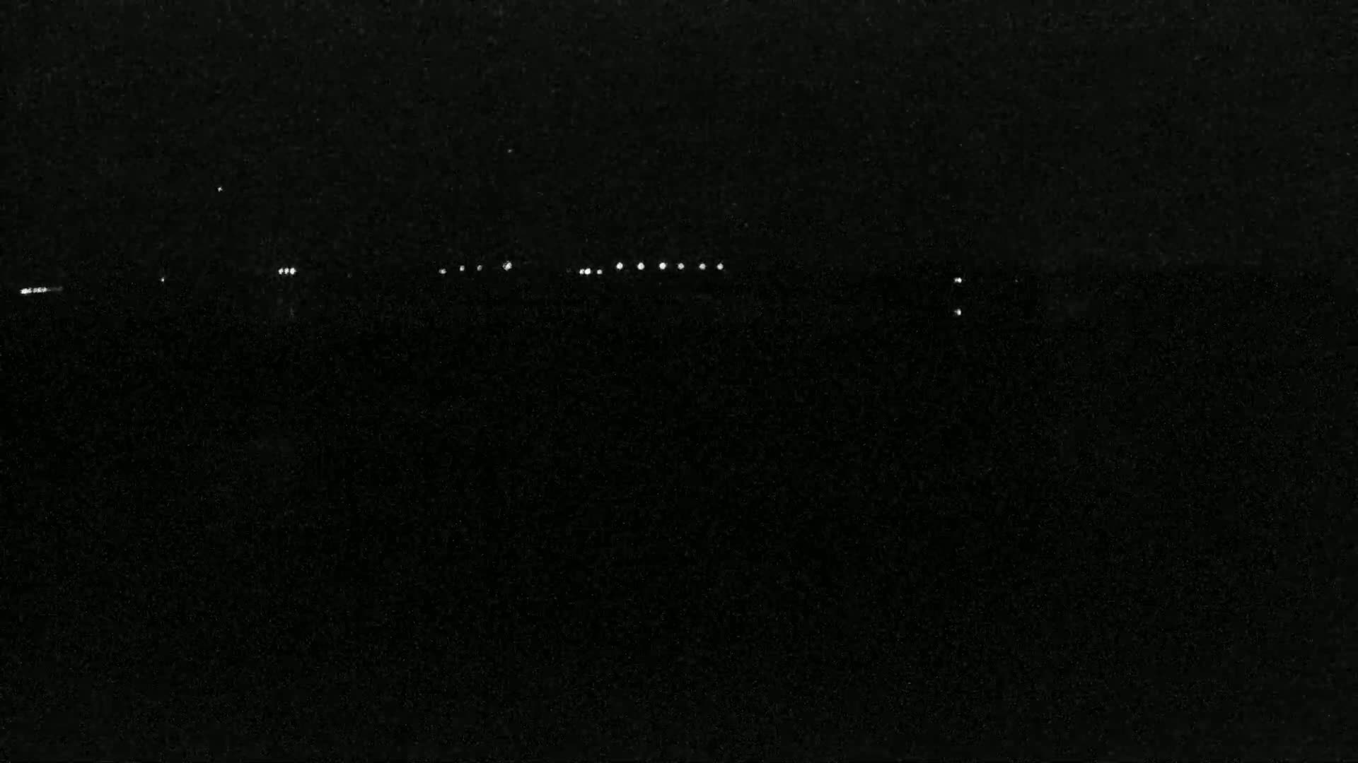 A dark, nighttime scene shows a line of distant lights on the horizon.