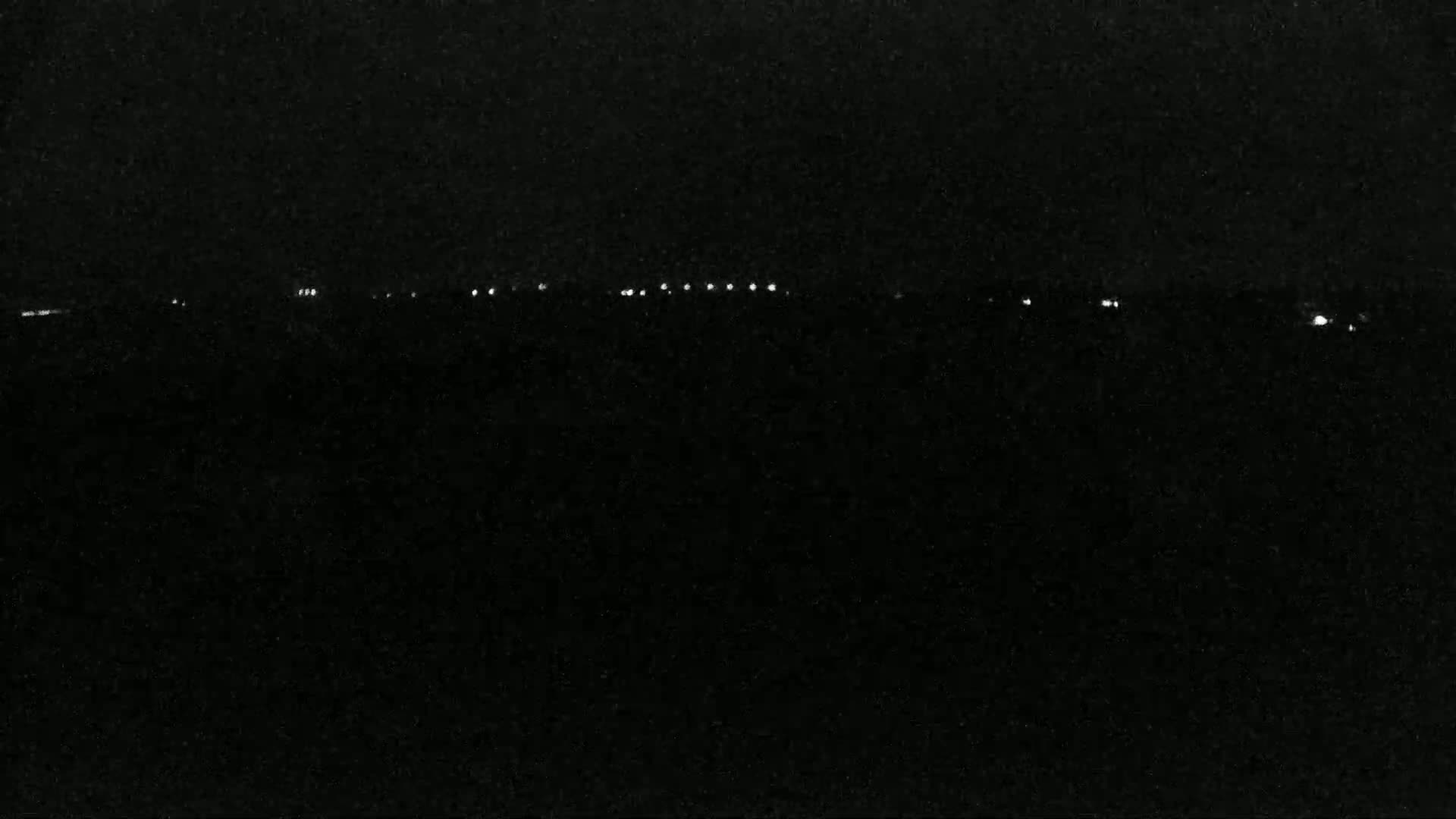 A nighttime view shows a line of distant lights against a dark, possibly cloudy sky.