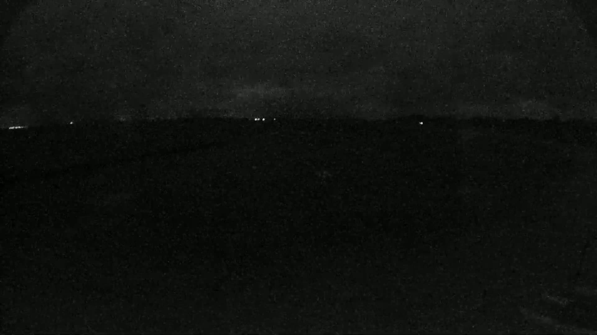 A dark, nighttime landscape is visible, showing a few faint lights on the horizon under a mostly cloudy sky.