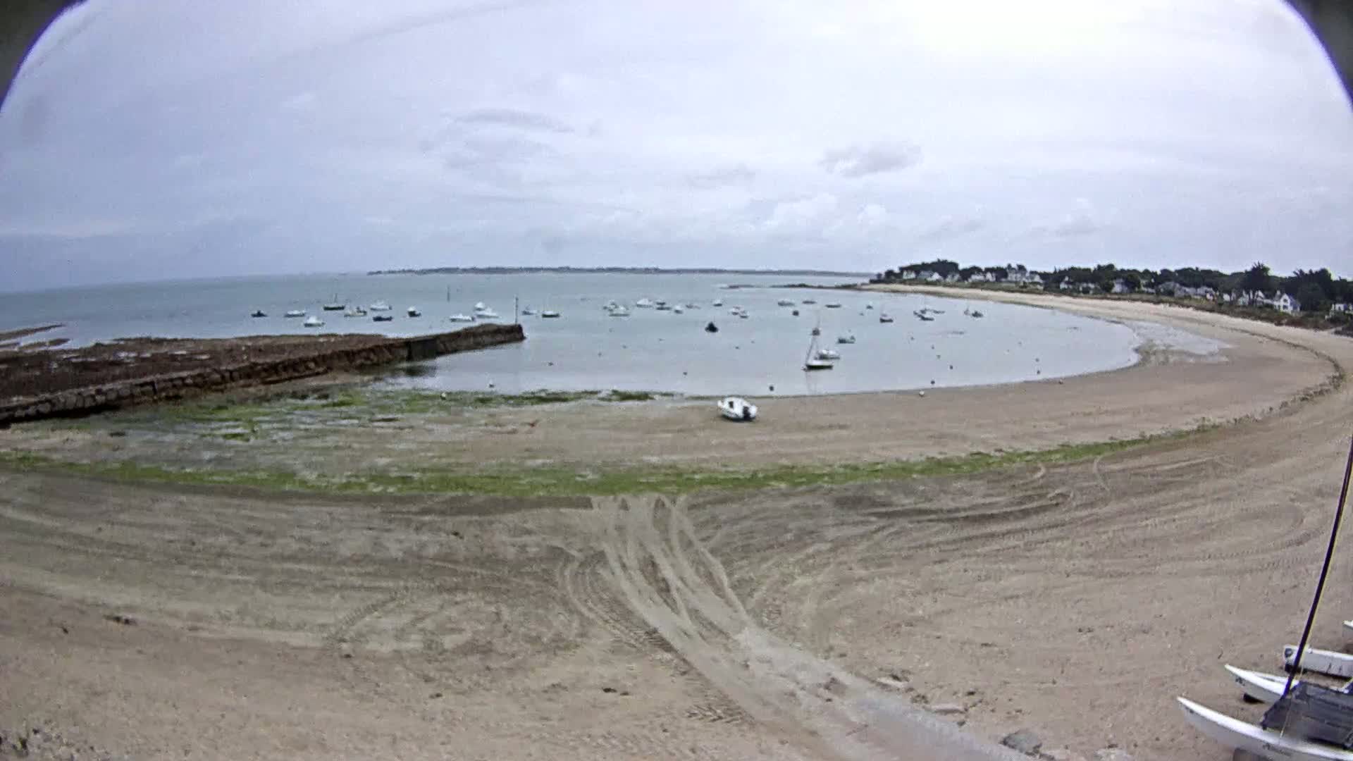 A sandy cove with several small boats in the calm water under an overcast sky.