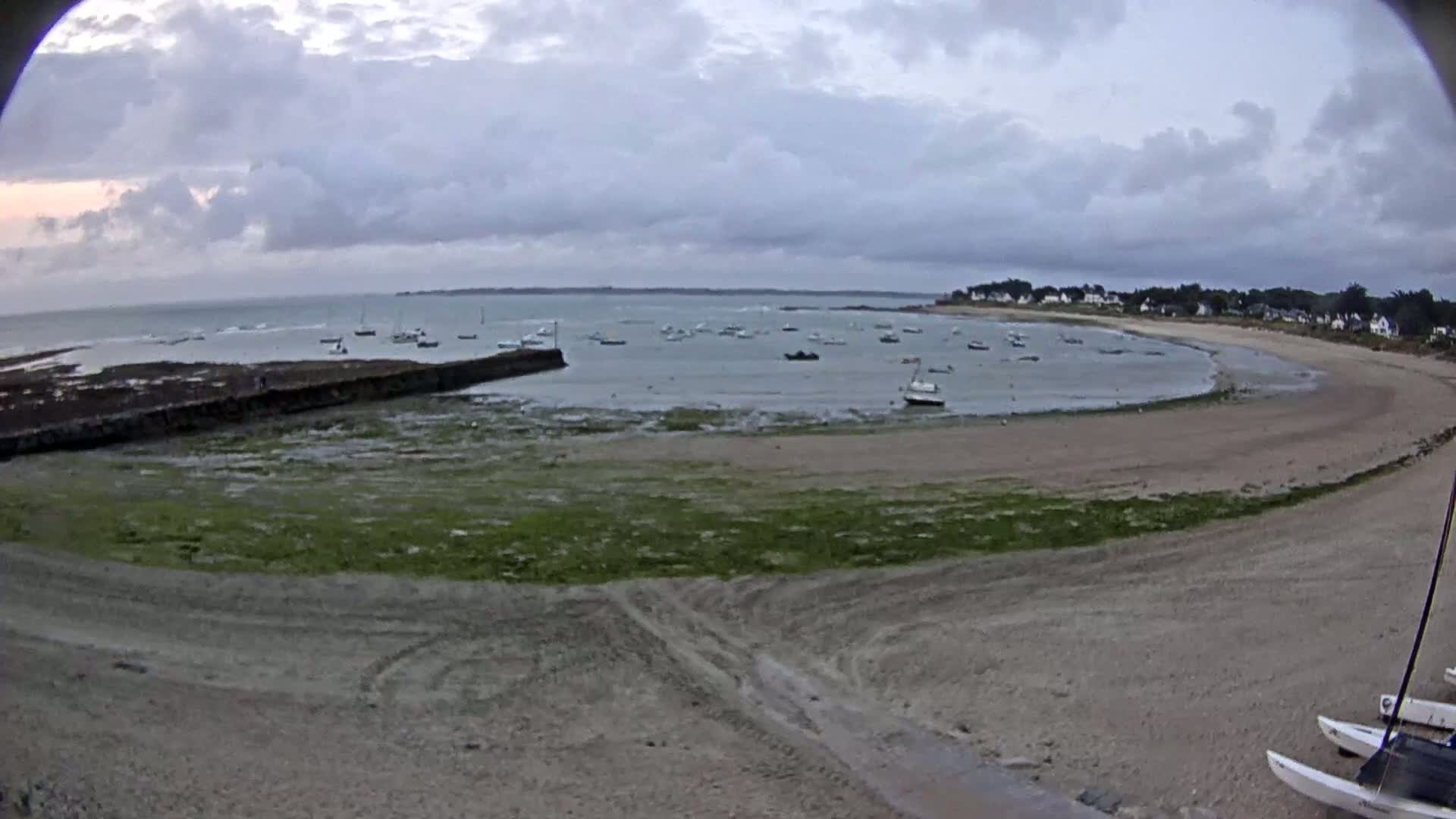 A sandy cove with several boats in the calm water under a cloudy sky.