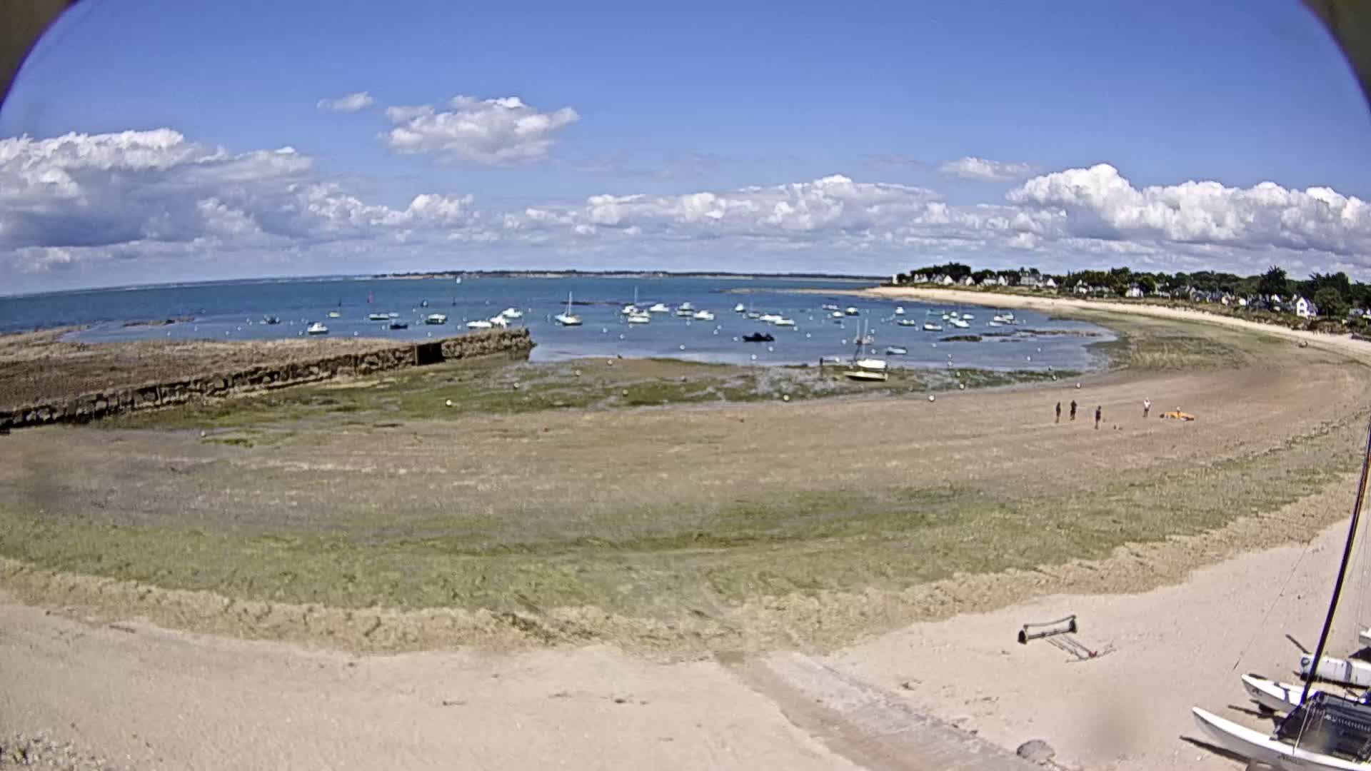 A sandy beach with several boats in the calm water under a partly cloudy blue sky.