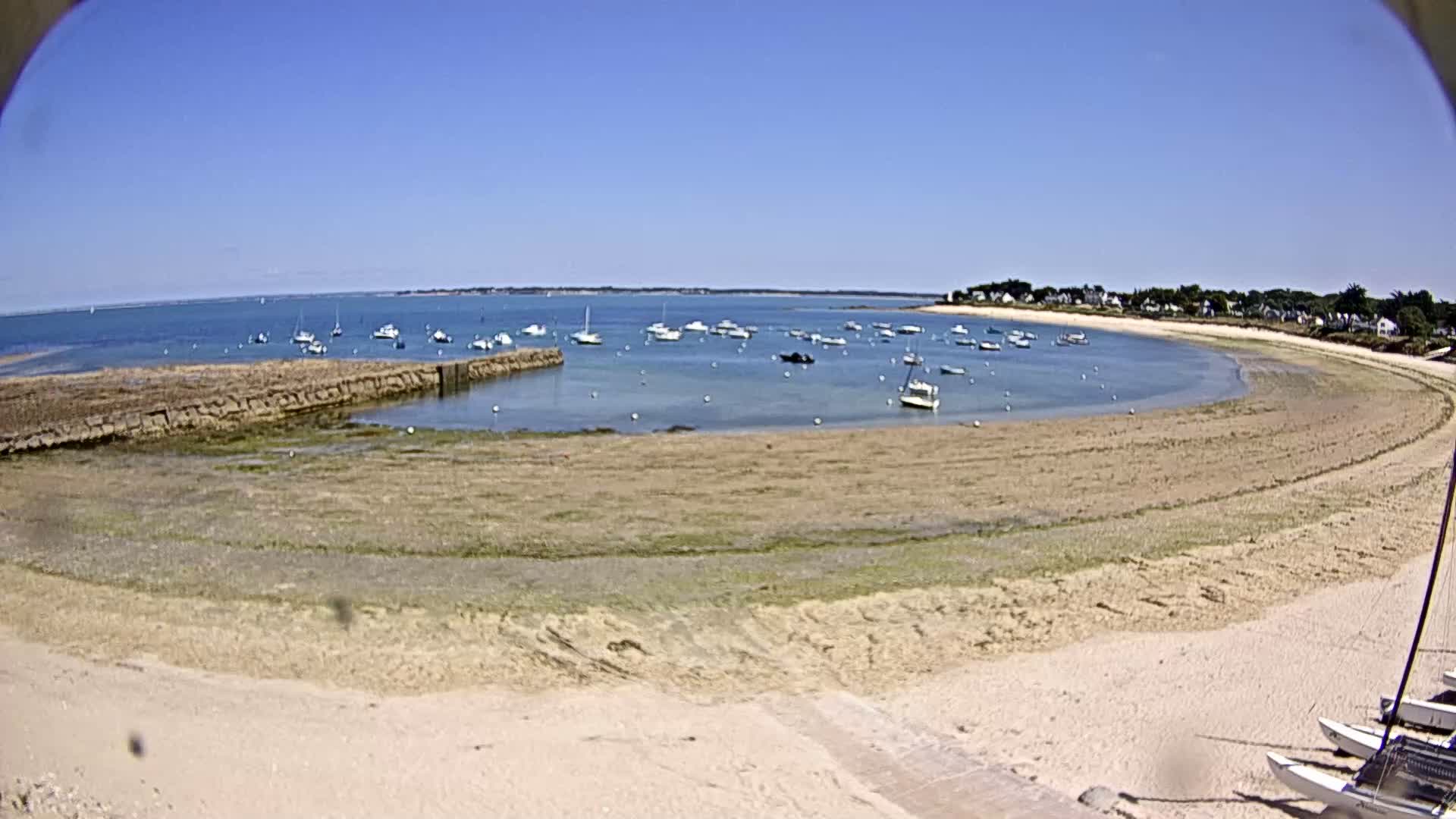A sandy cove with numerous small boats in calm, clear water under a bright blue sky.