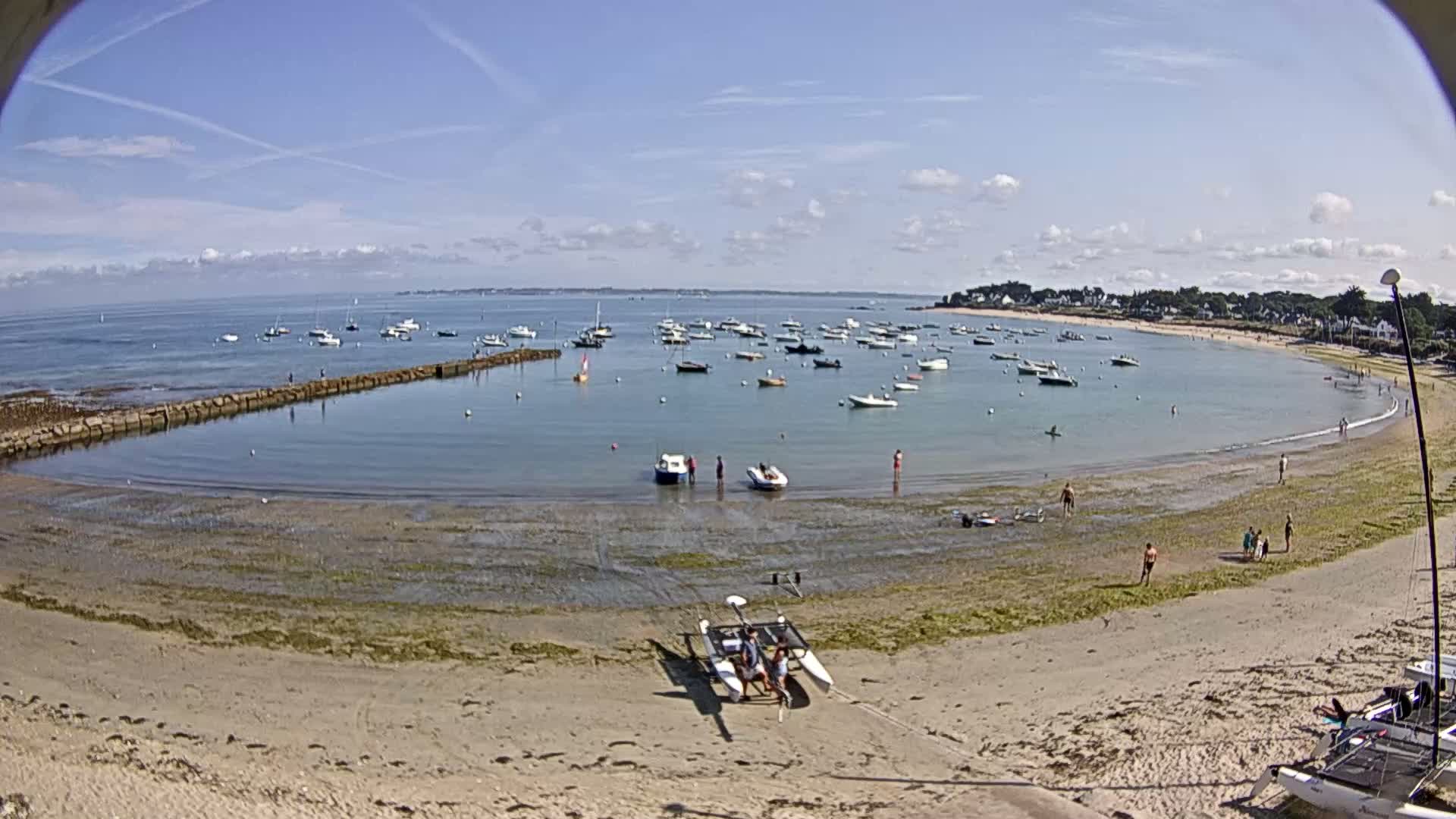A sandy beach with several small boats in a calm bay under a mostly sunny sky.