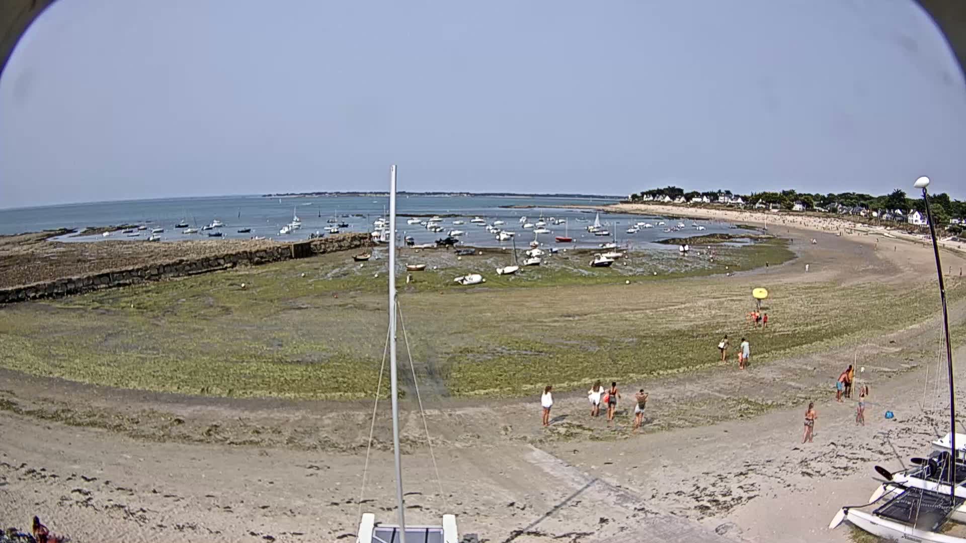 A sandy beach with several small boats in a calm bay under a mostly sunny sky.