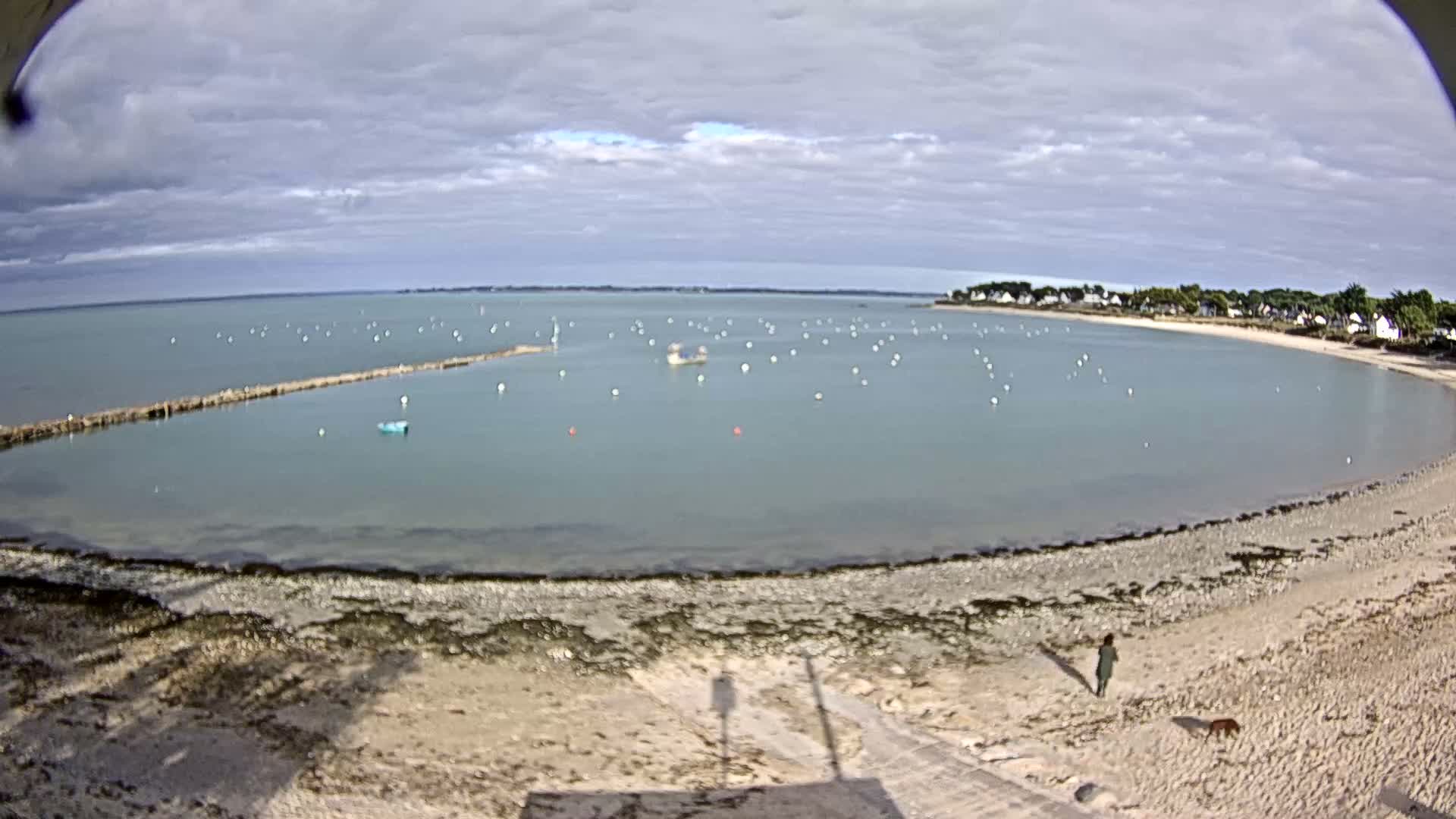 A sandy beach with several small boats in a calm bay under a mostly sunny sky.