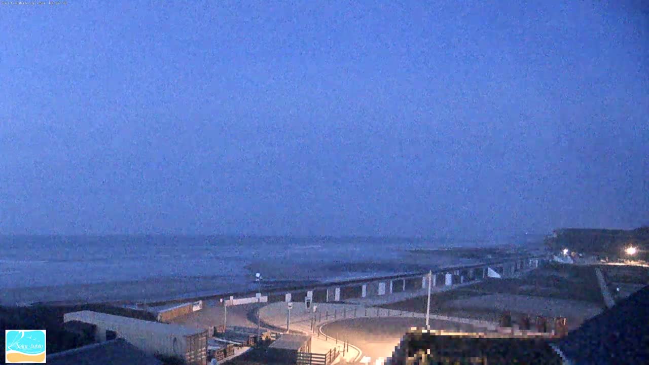 A beach at dusk, with a calm sea and a paved area leading down to the sand.