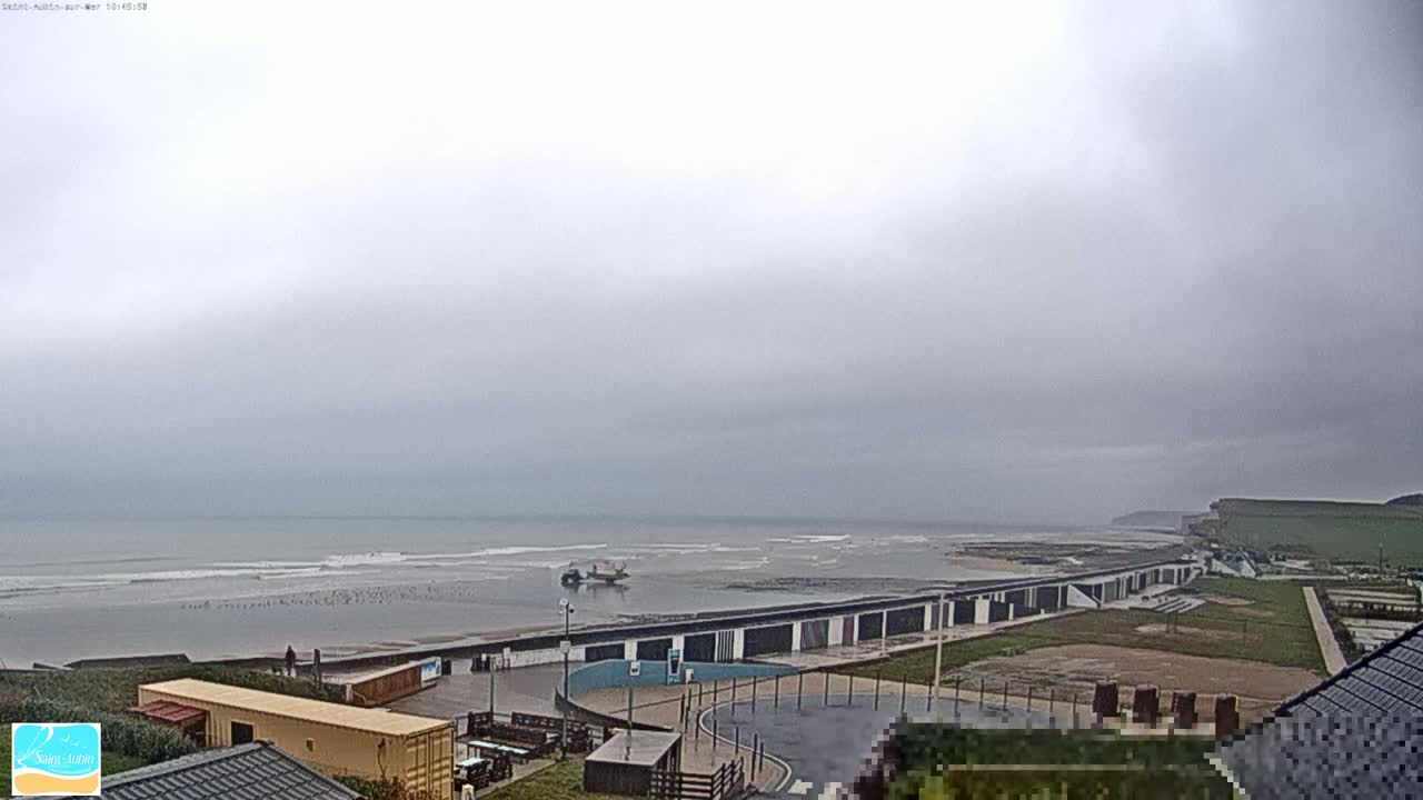 A mostly overcast day reveals a coastal scene with a calm sea, a long row of beach huts, and a small boat near the shore.