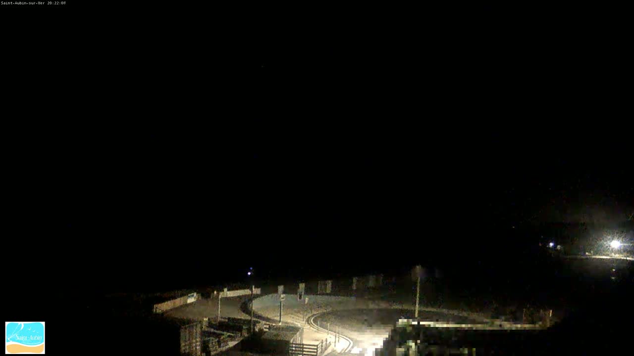 A nighttime, dimly lit, elevated view of a curving roadway with some surrounding structures under a dark sky.