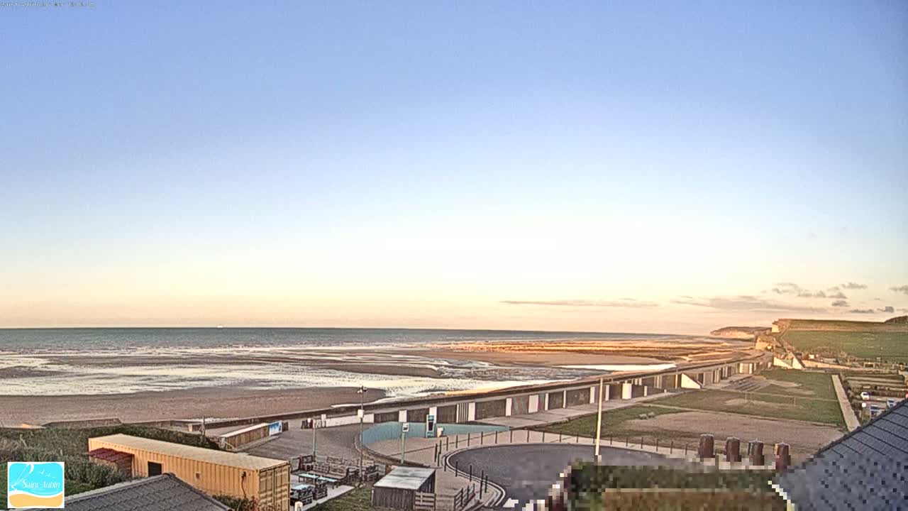 A wide, sandy beach stretches to a calm sea under a clear, pale-blue sunset sky.