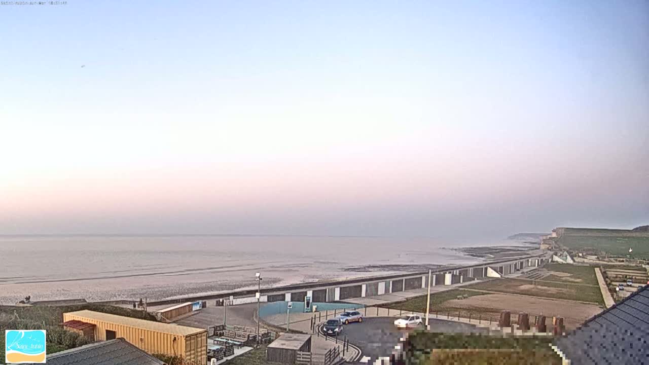 A wide, flat beach stretches to a calm sea under a pale pink and blue sky.