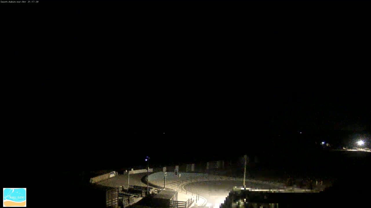 A nighttime, dark view of a paved area curving around a structure, illuminated by artificial light.