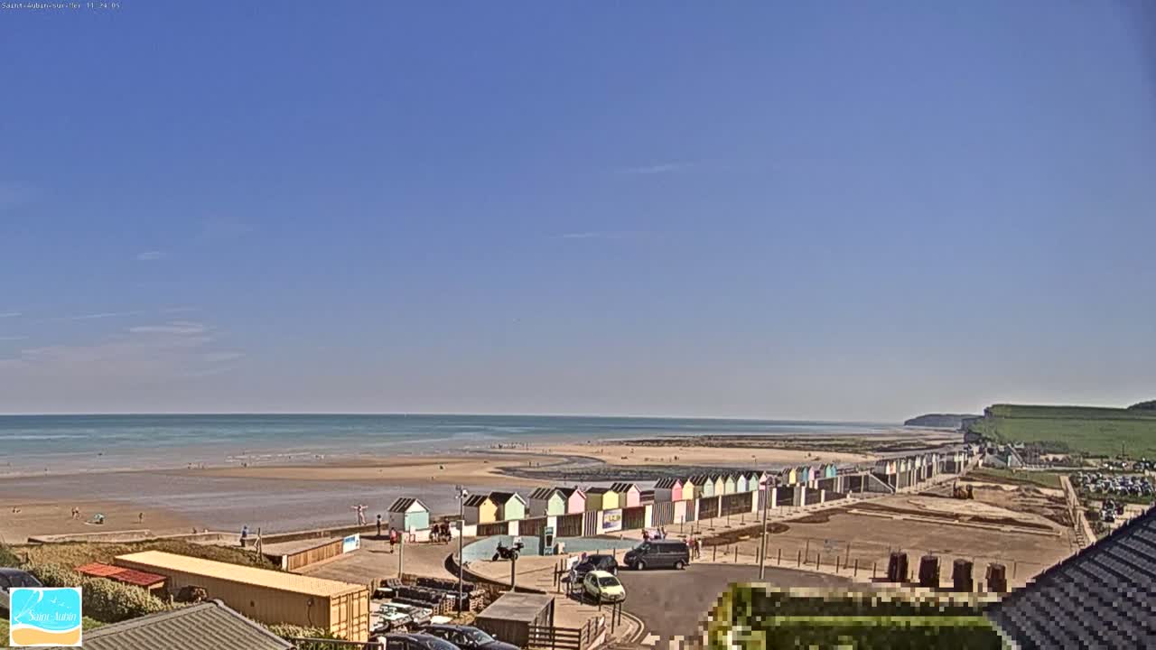 A row of colorful beach huts lines a sandy beach under a clear blue sky, with a calm ocean extending to the horizon.