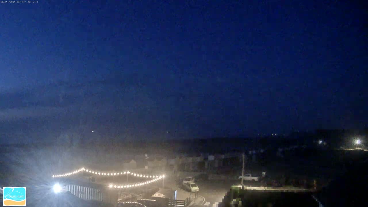 A nighttime, dimly lit coastal town scene under a dark blue sky with a few scattered lights visible in the distance.