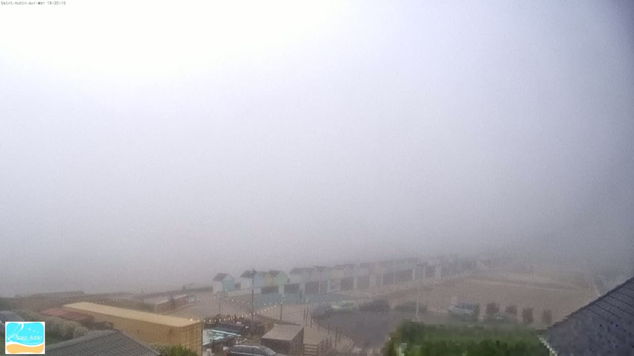 A foggy view of a beach with small buildings and a parking lot.