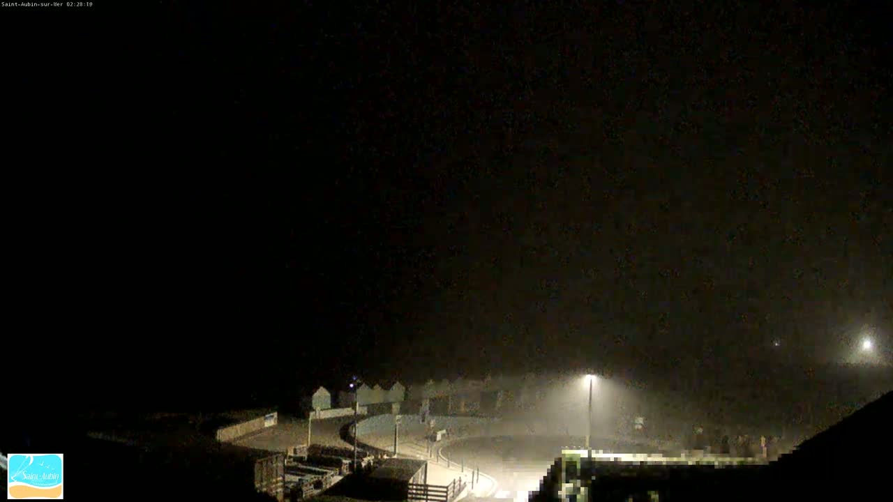 A foggy nighttime scene shows a row of beach huts and a curved roadway illuminated by streetlights.