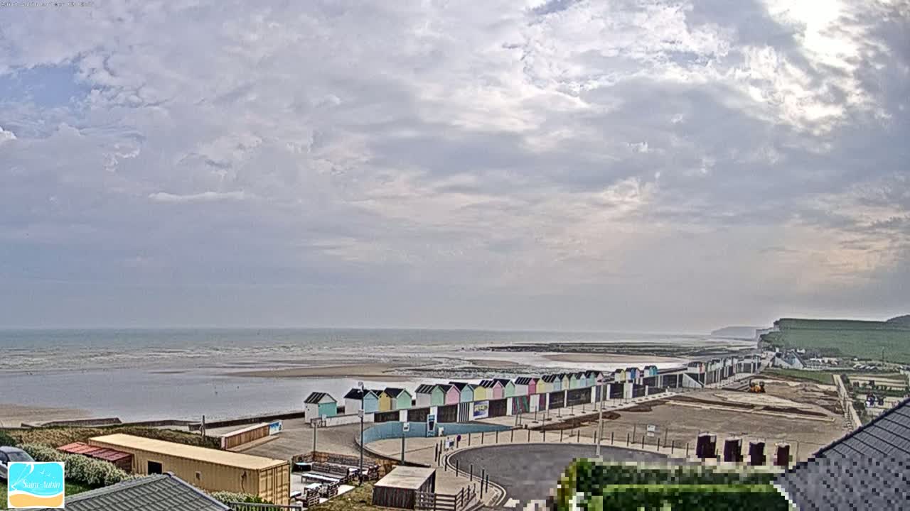 A row of colorful beach huts sits along a sandy beach, under a cloudy sky, overlooking a calm ocean.