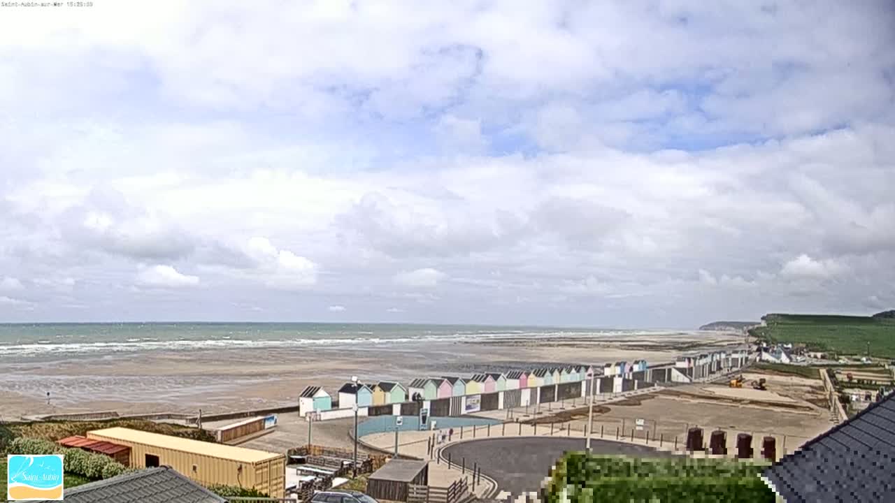 A row of colorful beach huts lines a sandy beach under a partly cloudy sky, with a calm ocean in the background.