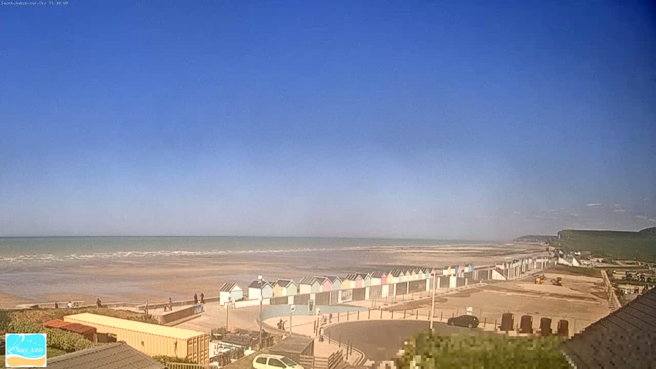 A row of colorful beach huts lines a sandy beach under a clear blue sky.