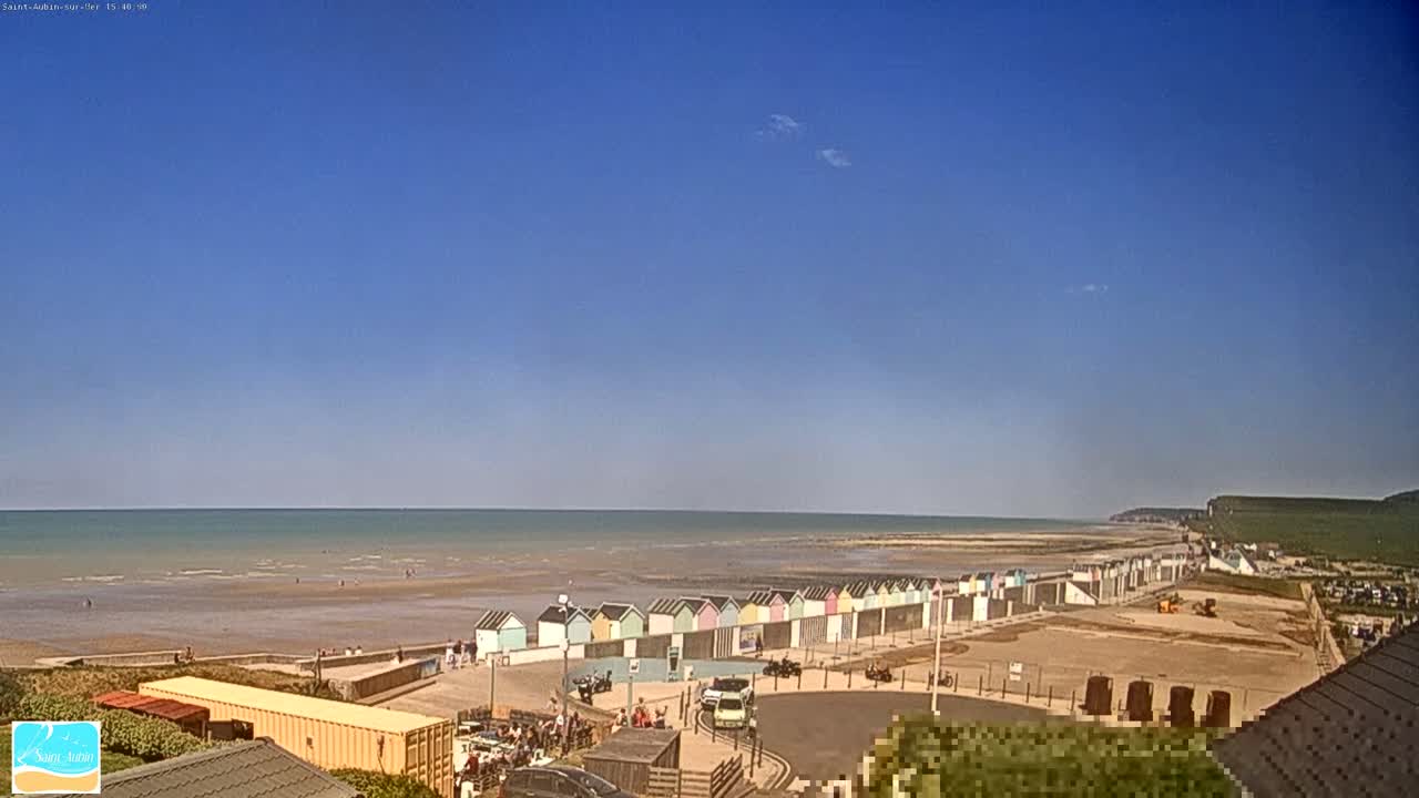 A row of colorful beach huts sits on a sandy beach next to a calm ocean under a clear blue sky.
