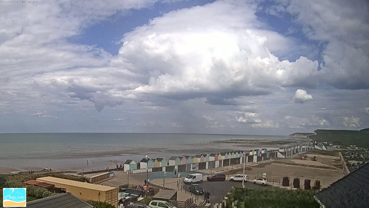 A partly cloudy day overlooks a beach with colorful beach huts, a calm sea, and a distant cliff.