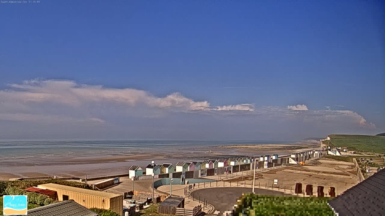 A row of colorful beach huts lines a sandy shore, overlooking a calm sea under a mostly clear sky with some scattered clouds.