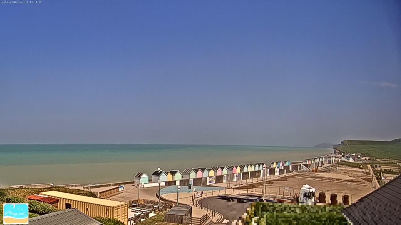 A row of colorful beach huts lines a calm, light-green ocean under a clear blue sky.