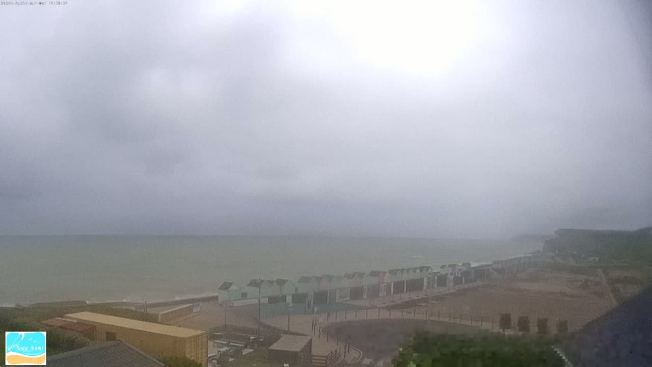 A row of beach huts sits on a coast overlooking a choppy sea under a heavily overcast sky.
