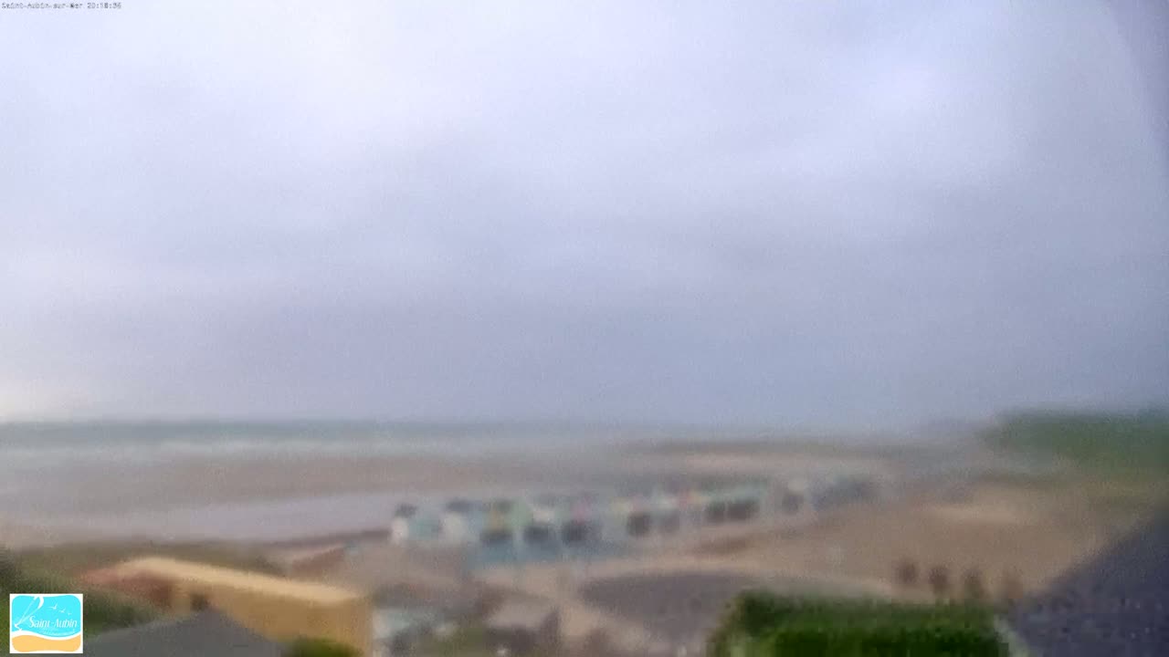 A hazy, overcast day reveals a beach with a row of low buildings, and a wavy ocean in the distance.
