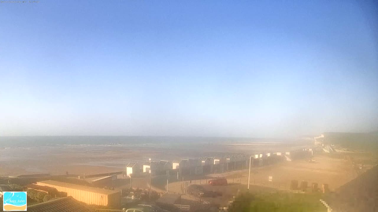 A hazy, sunny day reveals a beach with a row of small beach huts and a calm ocean in the distance.