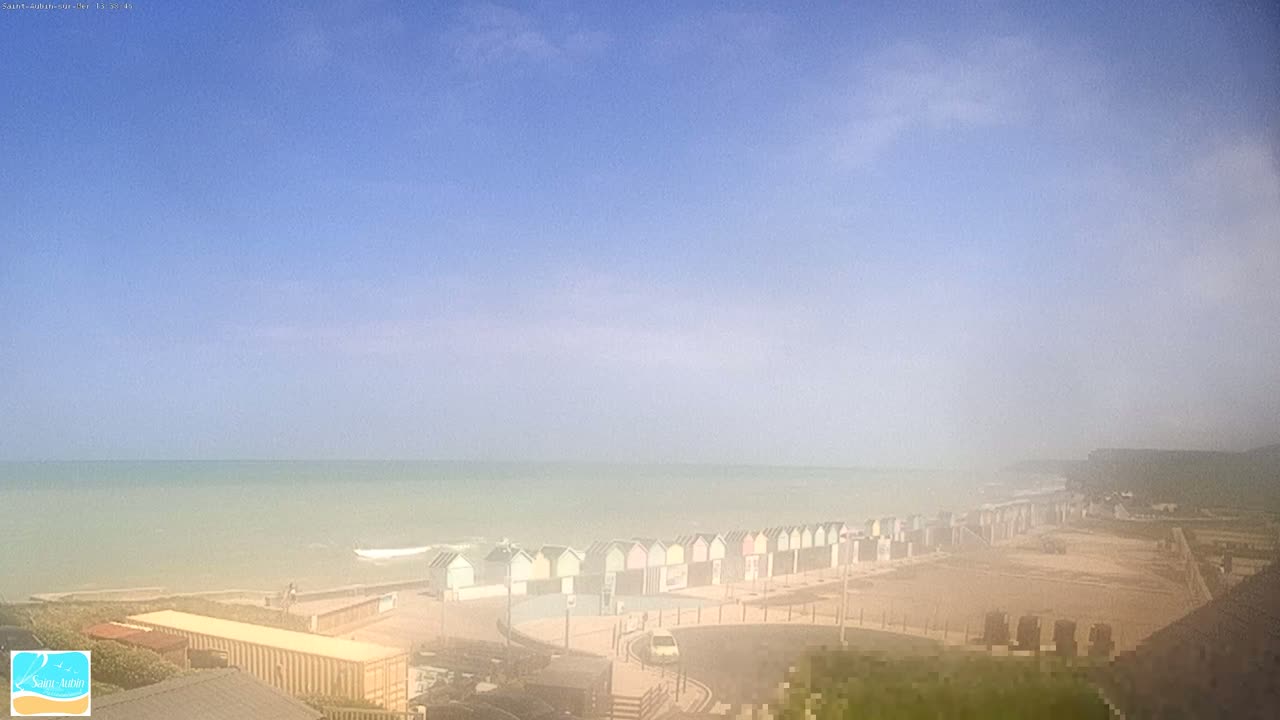 A hazy day at a beach with a row of beach huts and a calm sea.