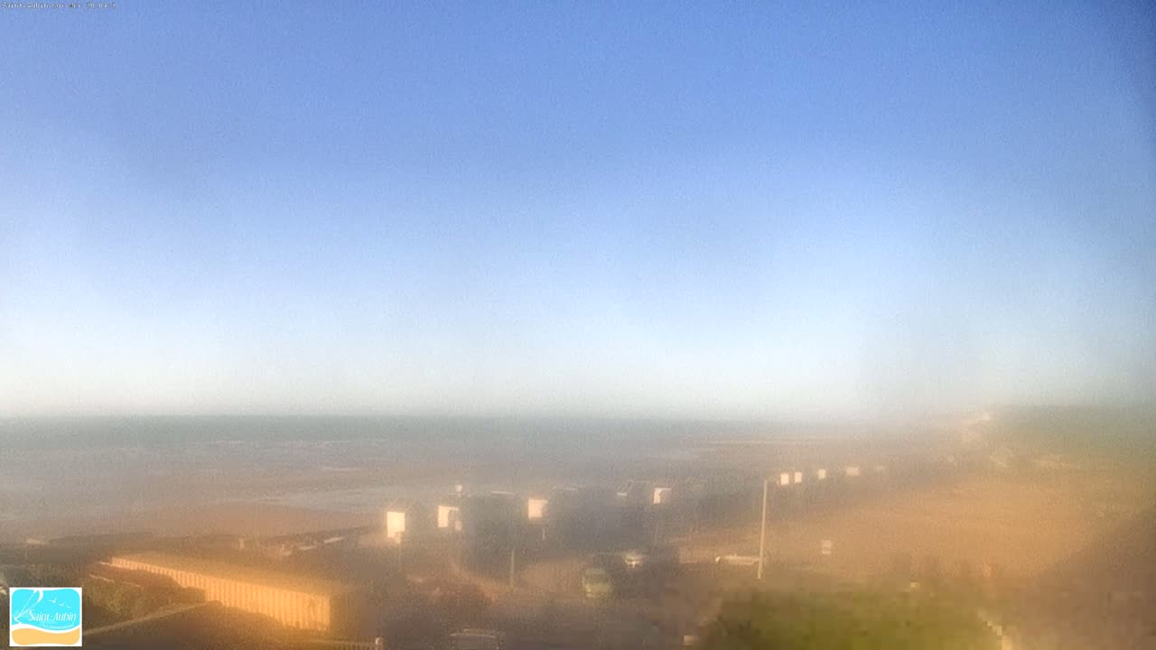 A hazy, long-distance view of a beach and ocean under a clear blue sky.