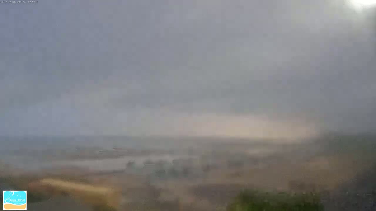 A hazy, overcast view of a flat coastal area with a body of water in the distance, possibly under light rain or mist.