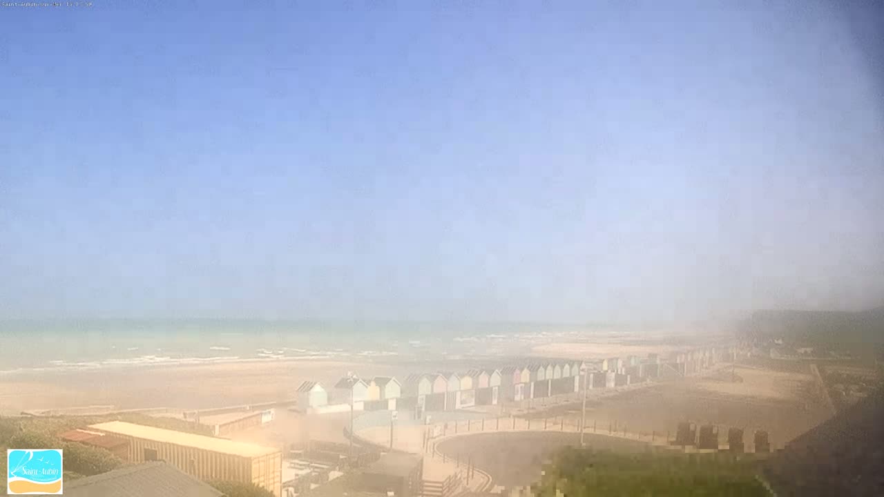 A hazy, sandy beach with a row of colorful beach huts is visible under a clear blue sky.