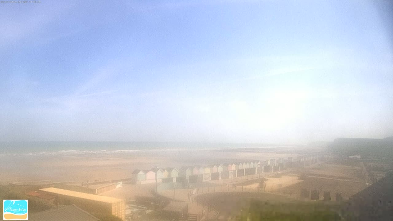 A hazy view shows a sandy beach with pastel-colored beach huts under a pale blue sky.