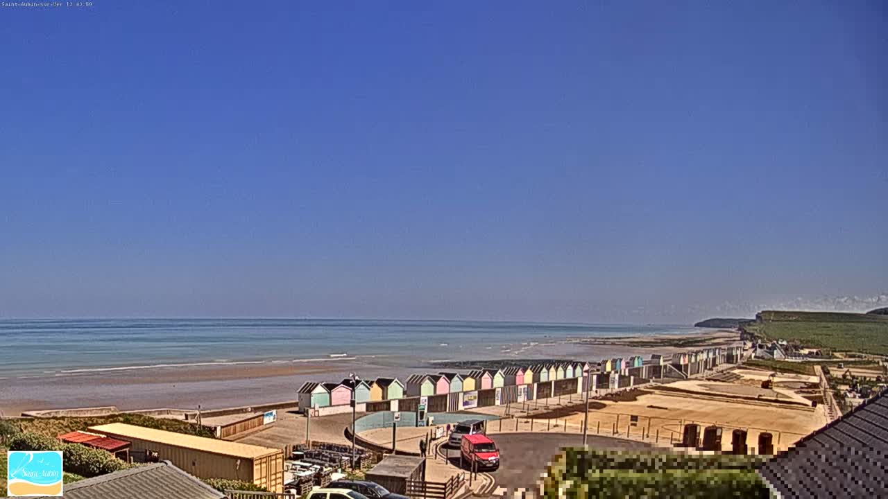 A row of colorful beach huts lines a sandy shore next to a calm ocean under a clear blue sky.
