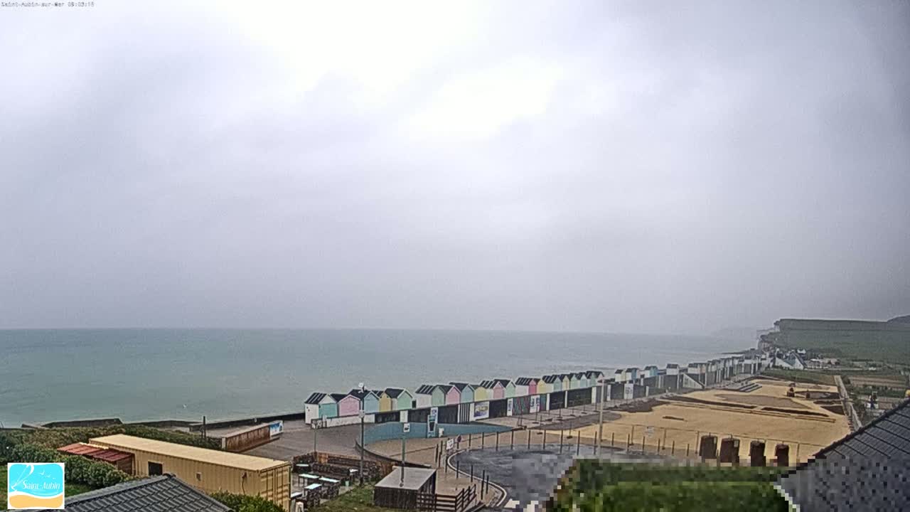A row of colorful beach huts lines a coastline under an overcast sky, overlooking a calm sea.