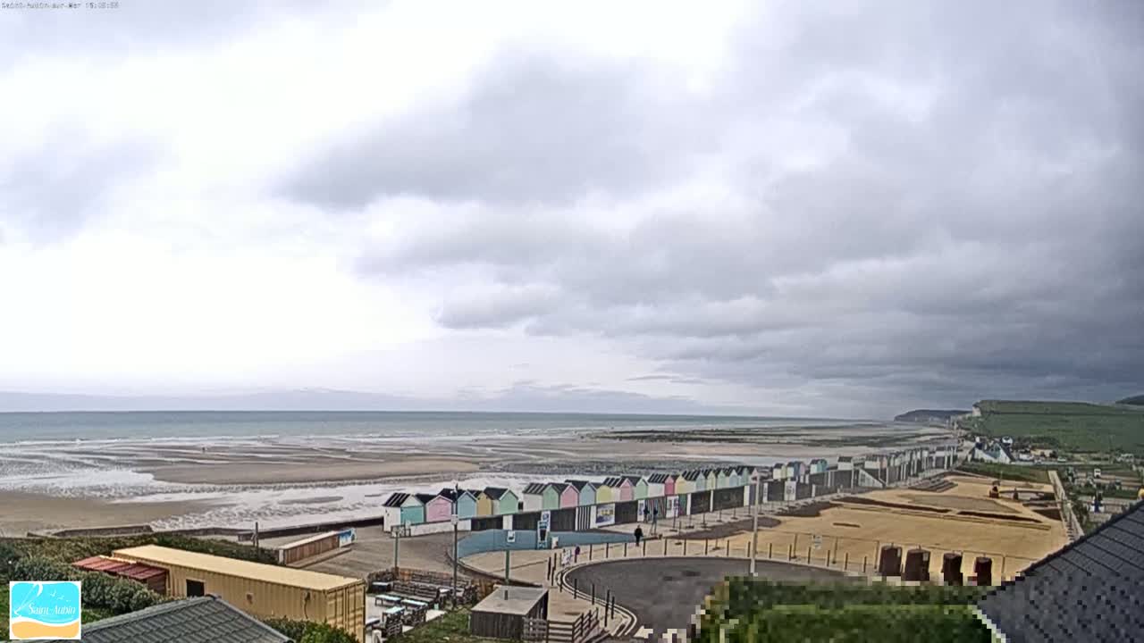 A row of colorful beach huts lines a sandy beach under a cloudy sky, with a calm ocean stretching to the horizon.