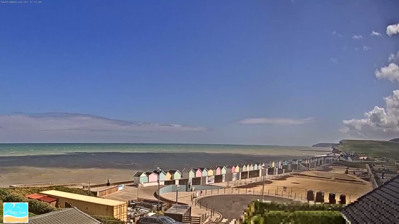A row of colorful beach huts sits on a sandy beach overlooking a calm sea under a mostly sunny sky with some scattered clouds.