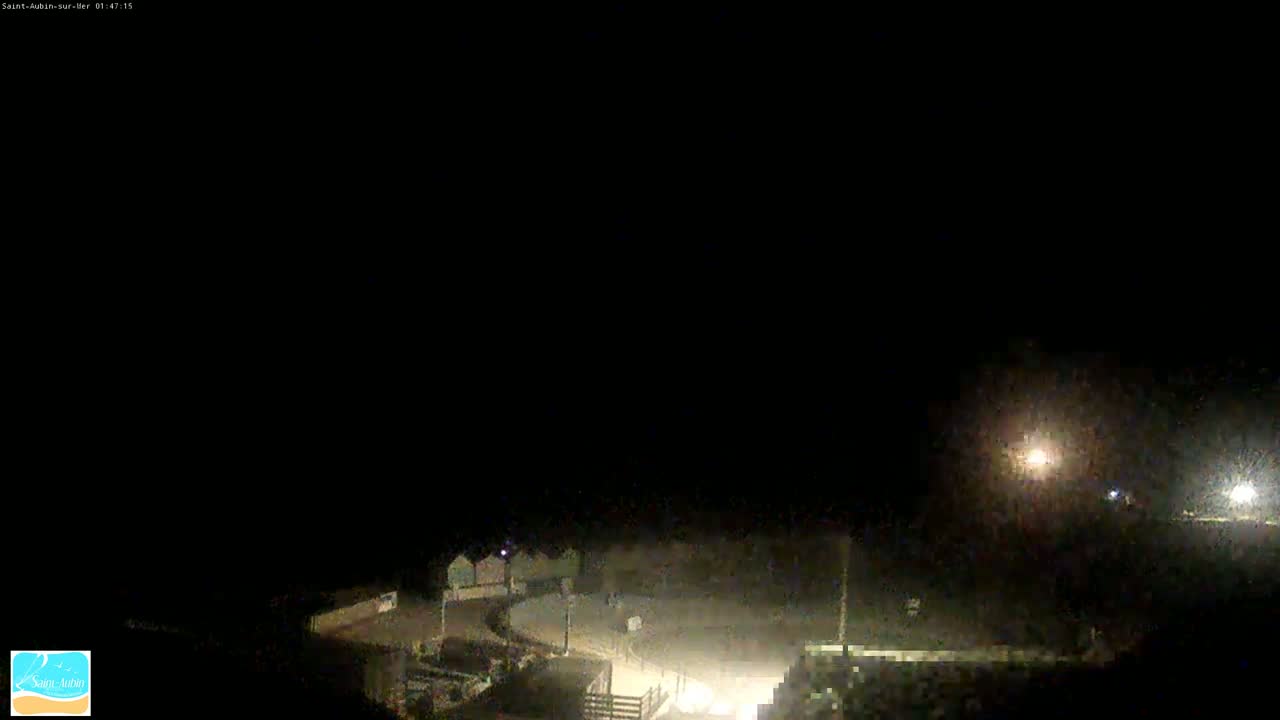 A dimly lit nighttime scene shows a mostly dark beach area with a few structures and lights visible.