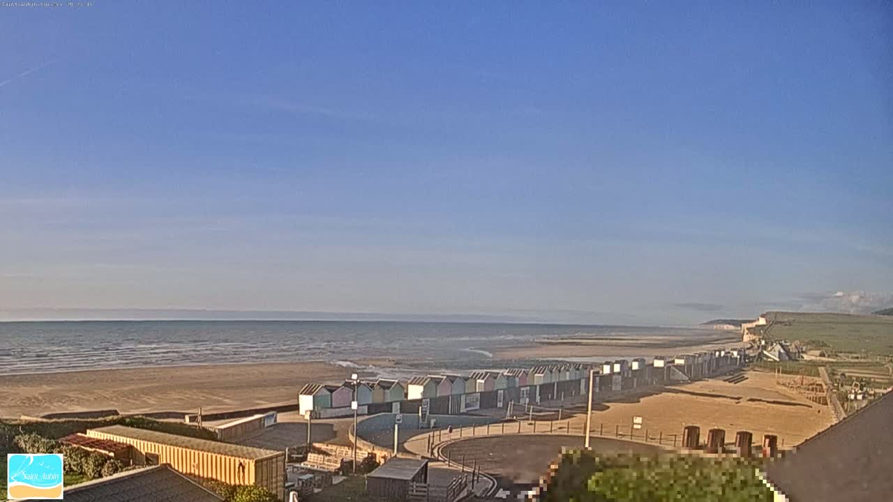 A row of colorful beach huts sits on a sandy beach next to a calm ocean under a clear blue sky.