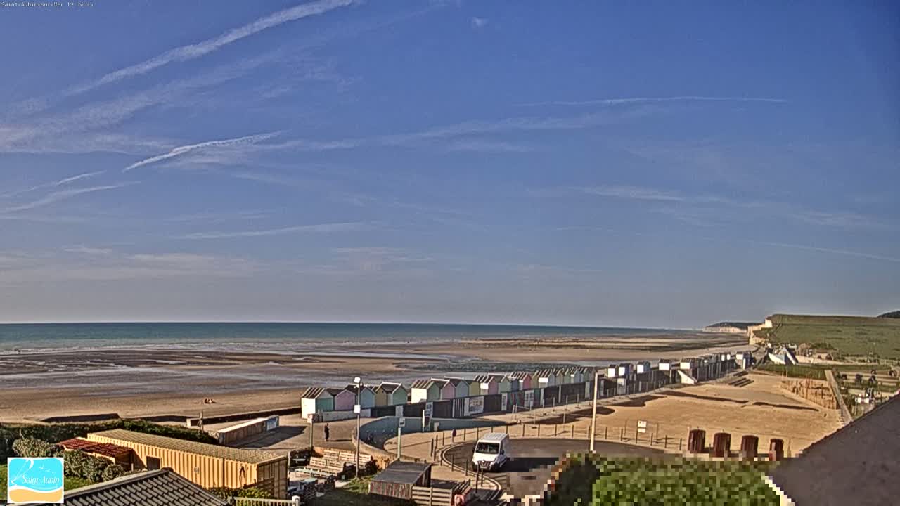 A beach with a row of colorful beach huts is visible under a mostly clear, blue sky with a few contrails.
